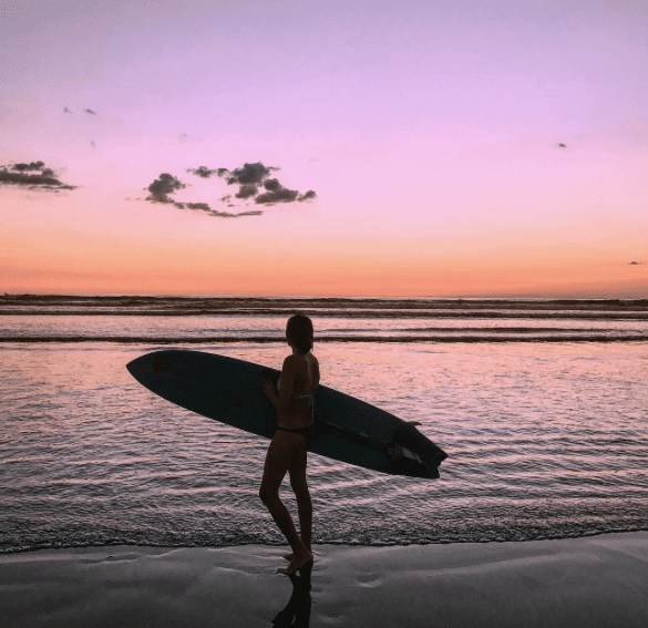 Girl with surfboard looking at sunset