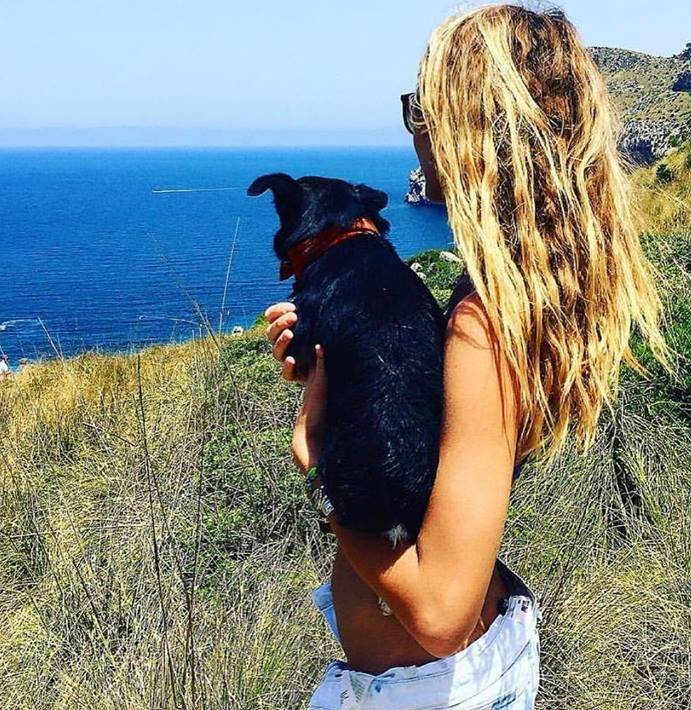 Blonde girl holding small dog overlooking the seaside in Mallorca